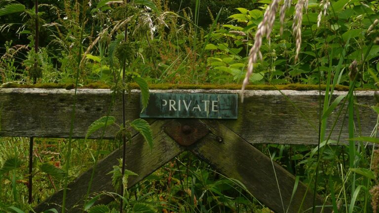 Old wooden gate with private sign in the middle blocking an overgrowth of greenery.